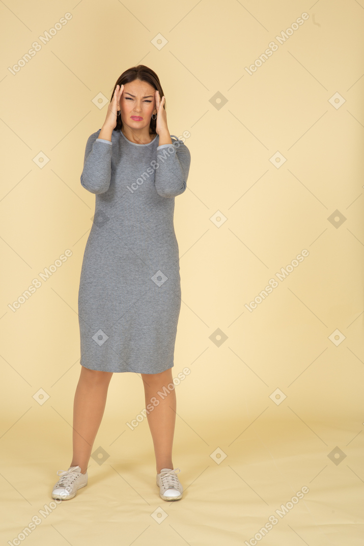 Vista frontal de uma mulher de vestido cinza sofrendo de dor de cabeça