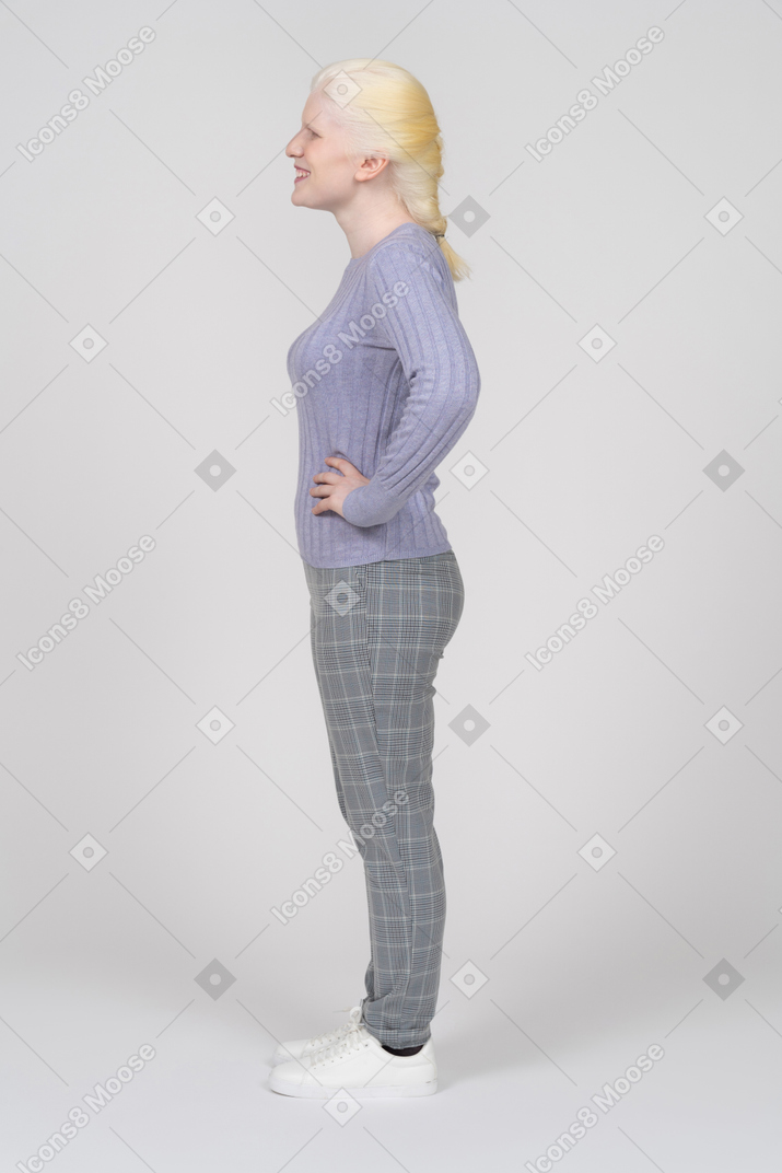 Vista laterale di una giovane donna allegra in piedi con le mani sui fianchi