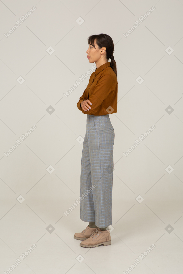 一位身着马裤和衬衫的年轻亚洲女性交叉双臂并展示舌头的侧视图