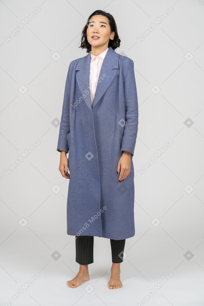 腕を両脇に置いて立っている青いコートを着た女性