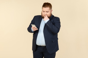 Duvidoso jovem homem com excesso de peso, segurando o smartphone