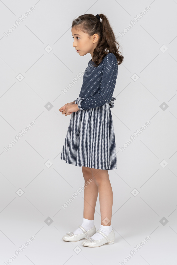 Vista lateral de una niña encorvada ligeramente mientras juguetea con los dedos