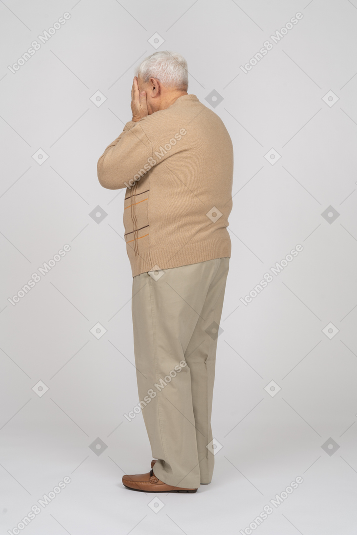 Seitenansicht eines alten mannes in freizeitkleidung, der das gesicht mit den händen bedeckt