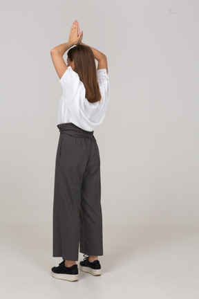 Vista posteriore di tre quarti di una giovane donna in abiti da ufficio che si tiene per mano sopra la testa