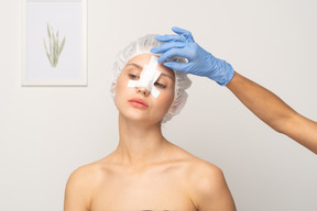 Doctor applying bandage to young woman's nose