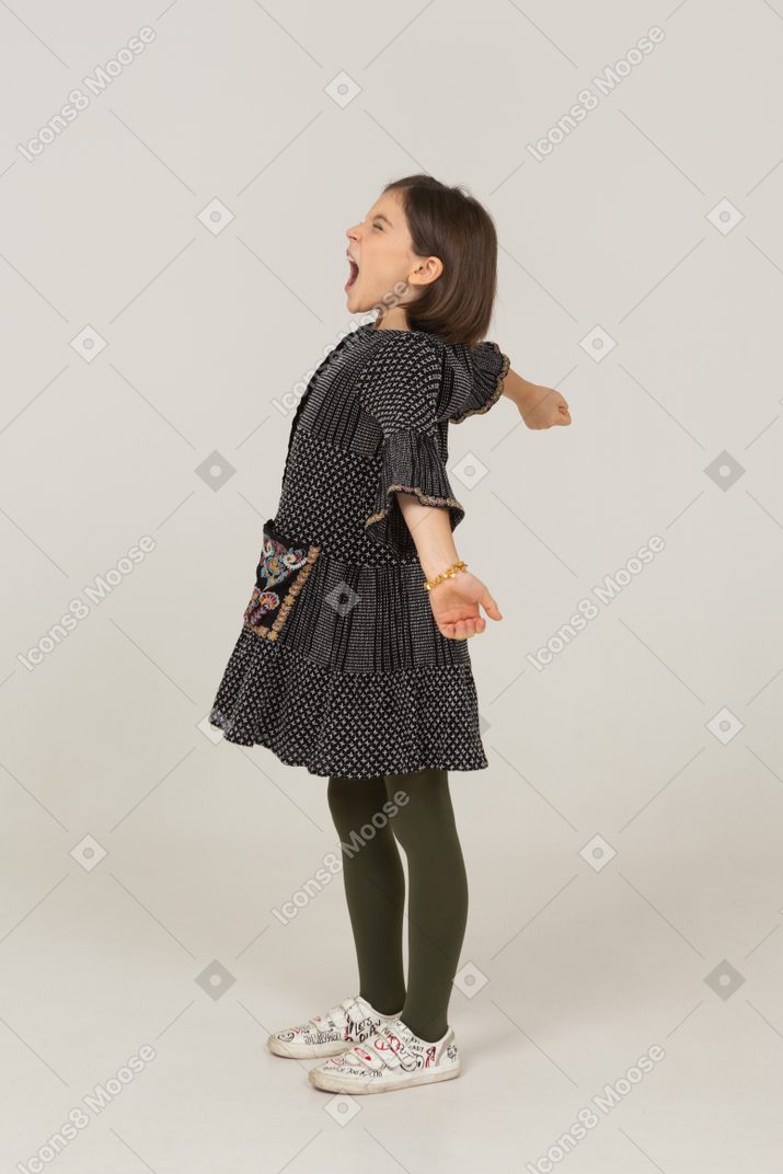 Vista laterale di una bambina che sbadiglia con un vestito che allarga le braccia