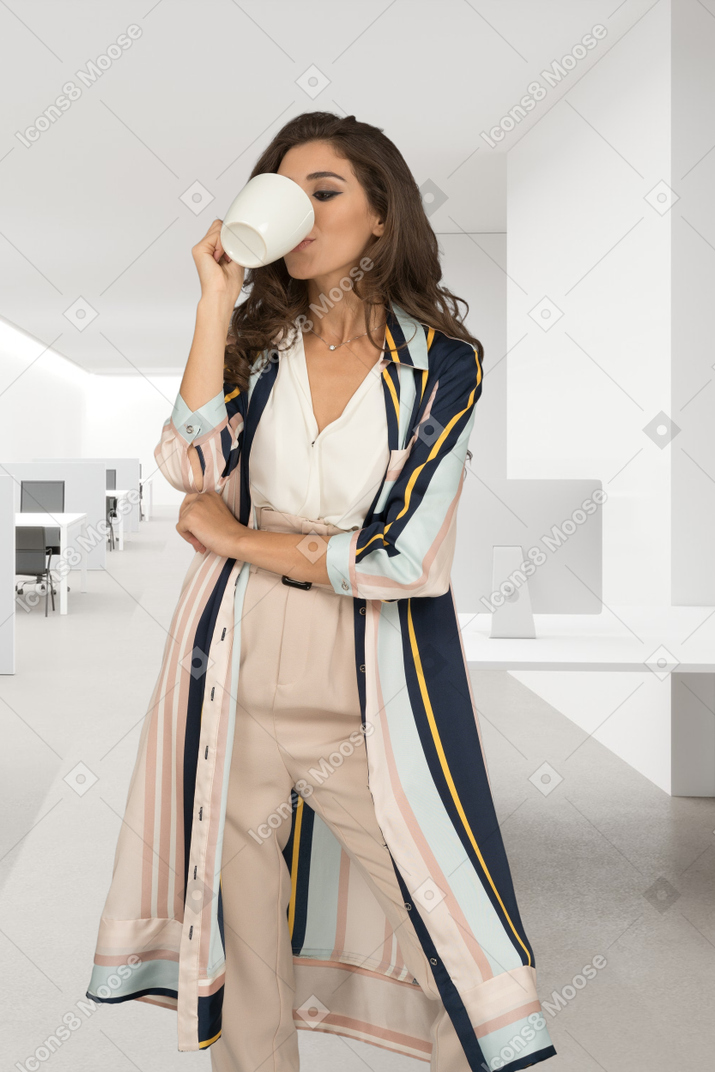 A woman standing in a room drinking from a cup