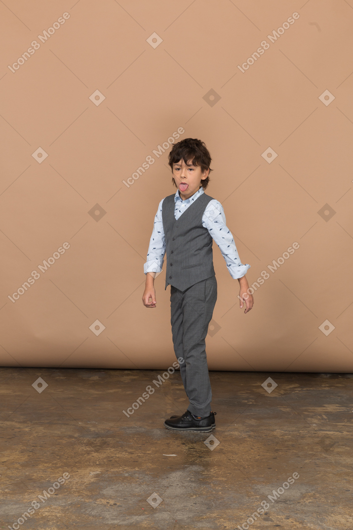 Cute boy in grey suit looking at camera and showing tongue