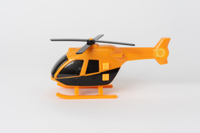 Helicóptero de brinquedo preto e laranja em pé contra um fundo branco liso