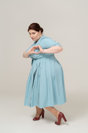 Vista lateral de uma mulher de vestido azul mostrando um gesto de coração