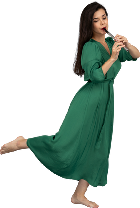 Вид сбоку на босую девушку в зеленом платье, играющую на флейте