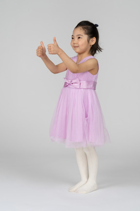 Портрет милой маленькой девочки, показывающей большие пальцы руки вверх