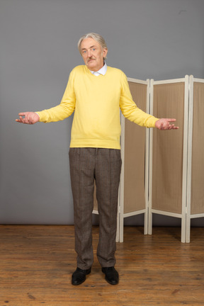 Front view of a perplexed old man raising hands looking at camera