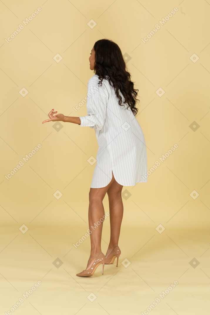 Vista lateral de una mujer joven de piel oscura interrogante con vestido blanco inclinado hacia adelante