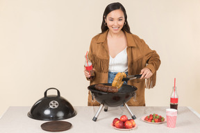 Joven mujer asiática sosteniendo una botella de coca cola y haciendo una barbacoa