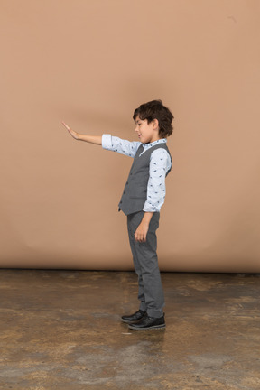 Vista lateral de um menino de terno cinza em pé com o braço estendido