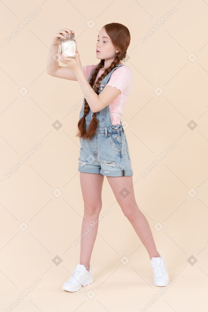 Surprised teenage girl looking at jar she's holding