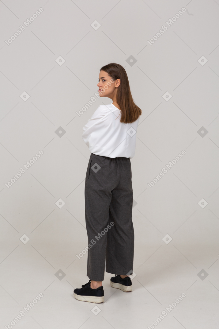 Vista traseira de três quartos de uma jovem zangada com roupas de escritório, cruzando os braços