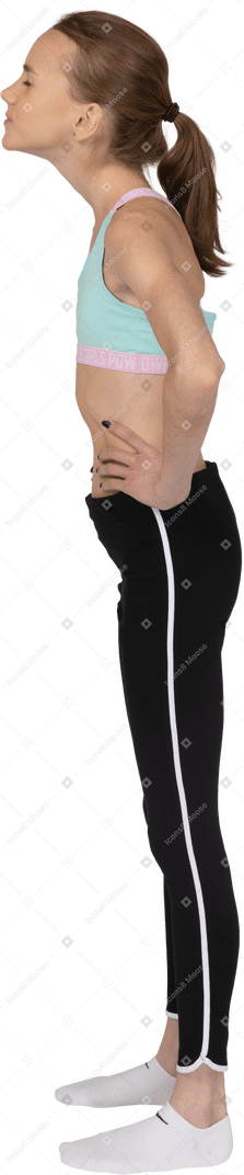 Vista laterale di una ragazza adolescente in abbigliamento sportivo che mette le mani sui fianchi con gli occhi chiusi