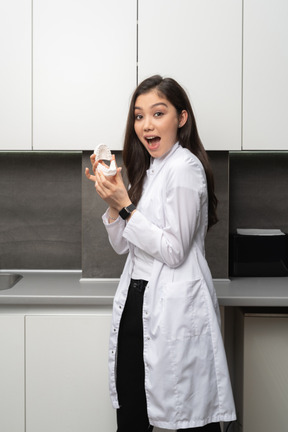 Close-up a surprised female dentist holding a jaws prototype and looking at camera