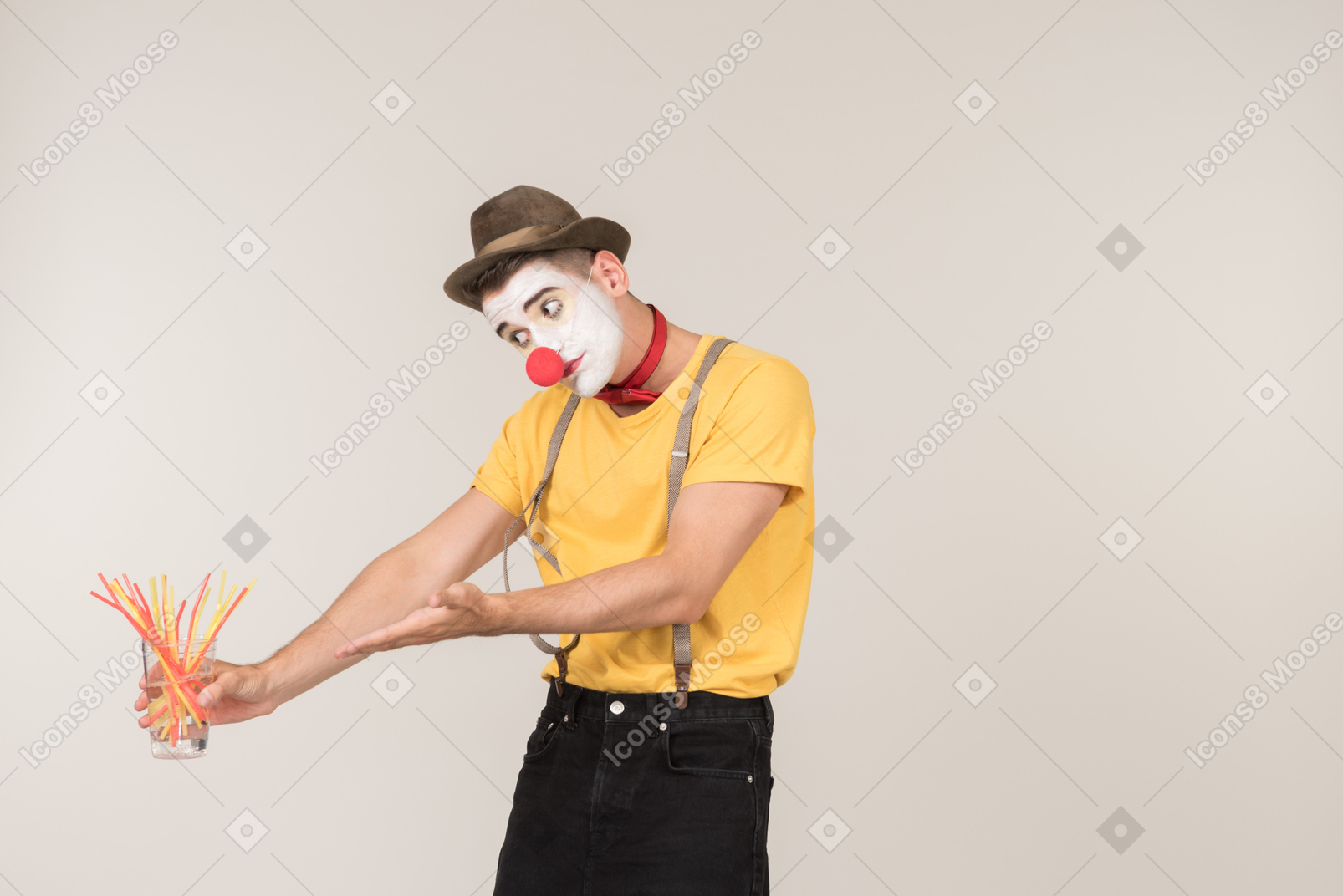 Sad male clown pointing at glass of plastic straws he's holding