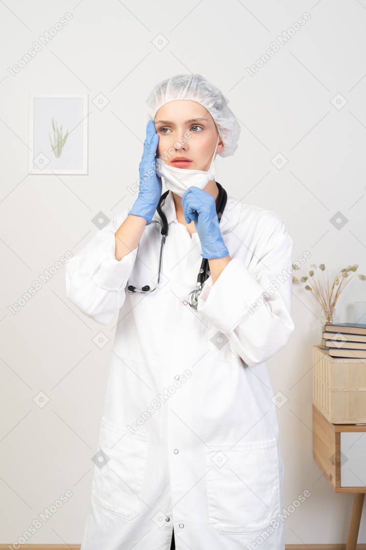 Vista frontal de una joven doctora poniéndose una máscara y mirando a un lado