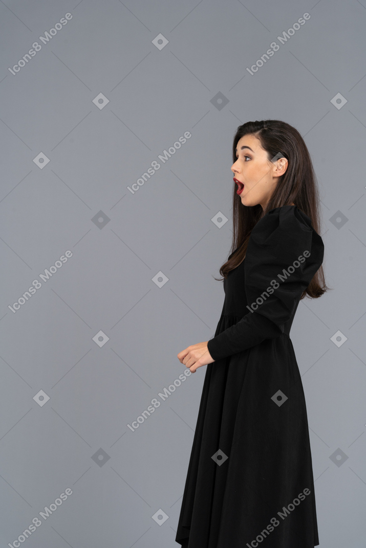 Side view of a surprised young lady in a black dress opening her mouth