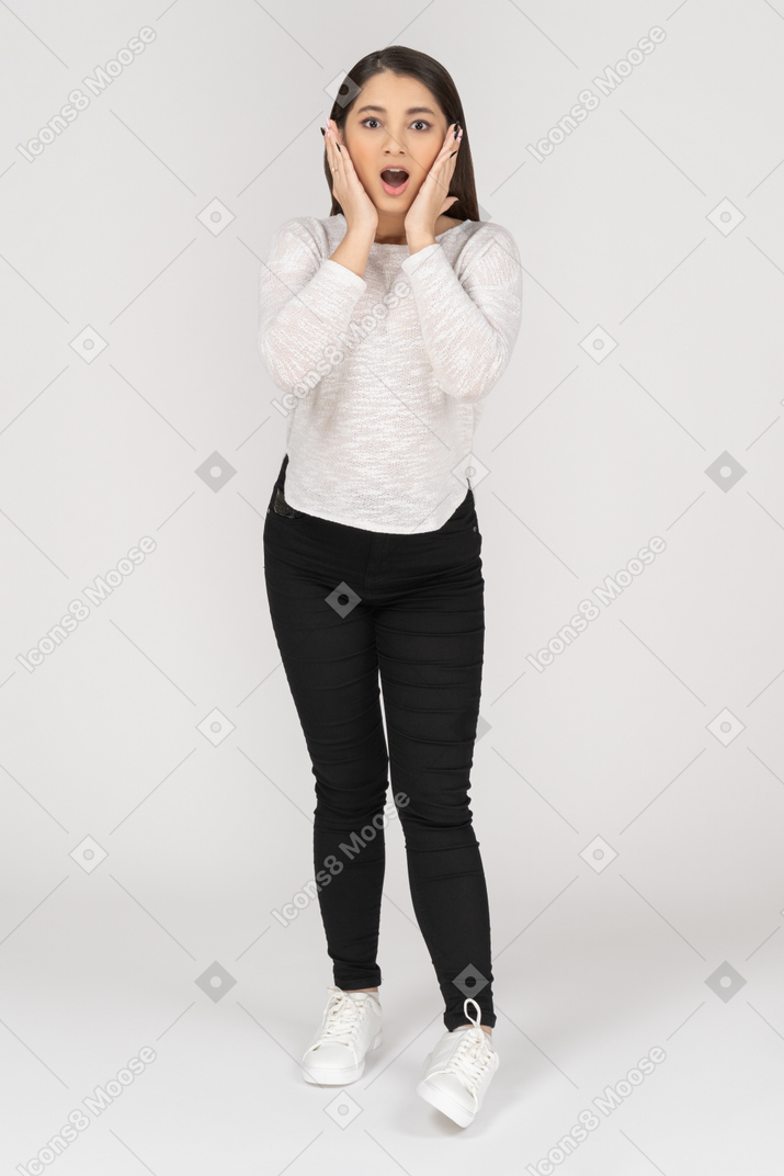 Front view of a shocked young indian female in casual clothes touching face