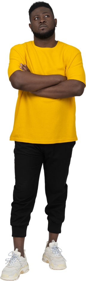 Vista frontale di un giovane uomo sospettoso dalla pelle scura con una maglietta gialla che incrocia le braccia