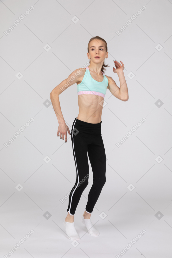Вид в три четверти девушки-подростка в спортивной одежде, поднимающей руки и сидящей на корточках