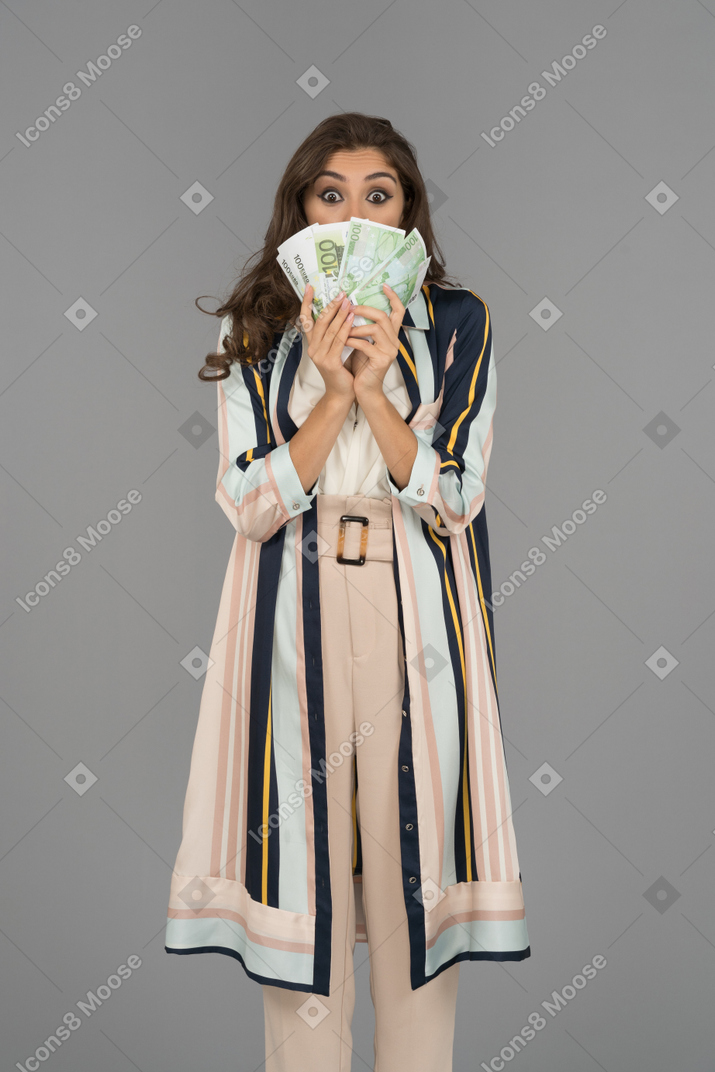 Surprised young woman covering her mouth and nose with a cash fan