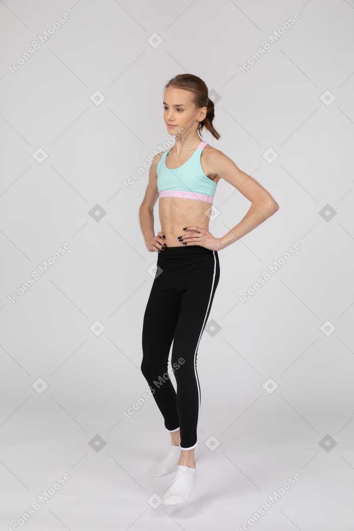 Vista de tres cuartos de una adolescente en ropa deportiva poniendo las manos en las caderas y dando un paso adelante