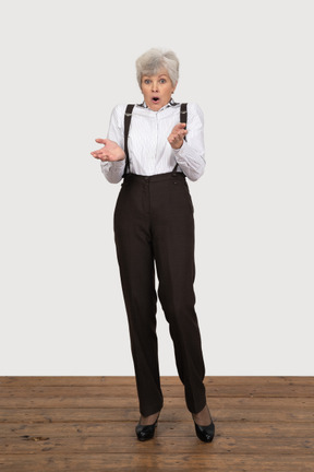 Front view of a surprised old lady in office clothing raising her hands