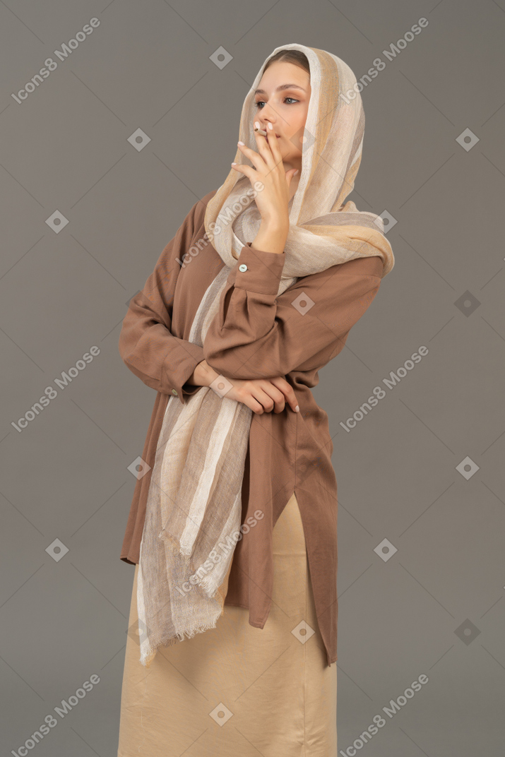 Three quarter view of a young woman in headscarf and beige clothes smoking a cigarette