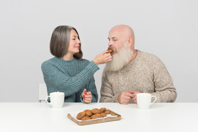 Gealterter mann, der plätzchen von den händen seiner frau isst