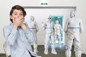 Boy covering mouth in front of a group of people in protective suits