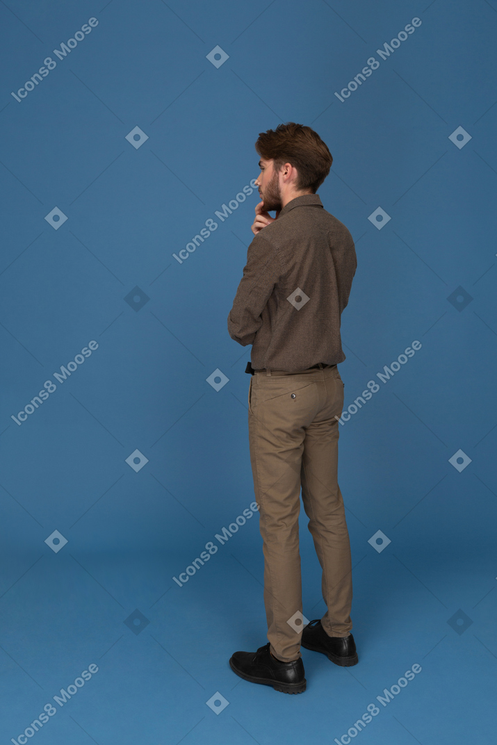 Стройный молодой человек, стоящий спиной к камере и касающийся его подбородка
