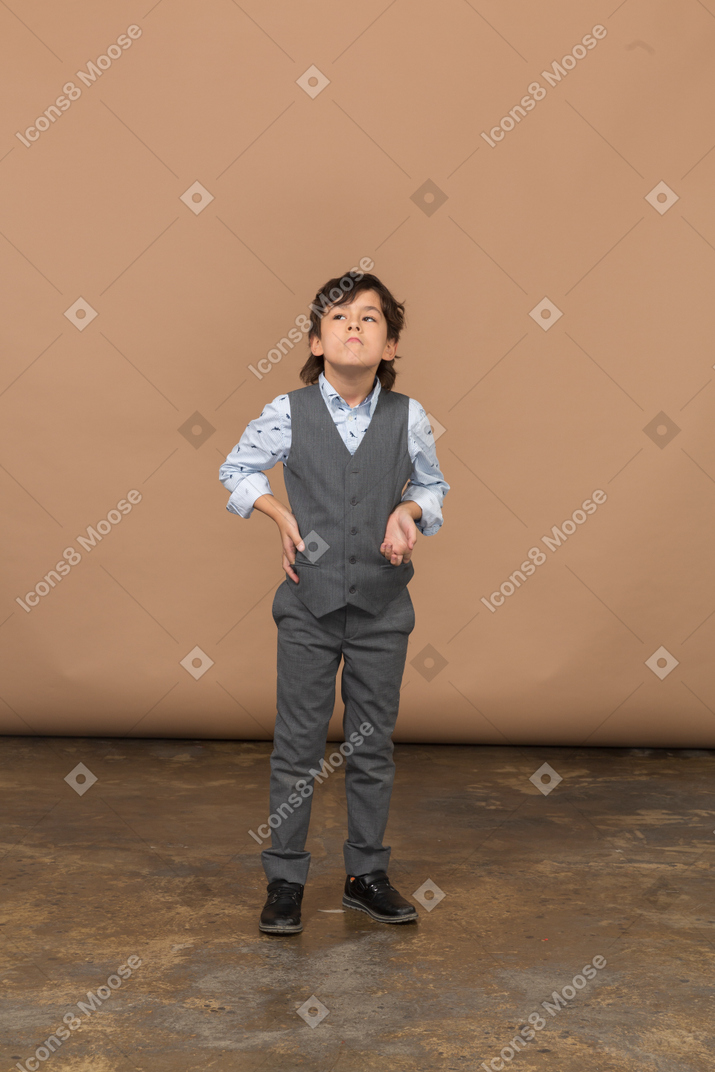 Vista frontal de un niño con traje gris posando con la mano en la cadera y mirando hacia arriba