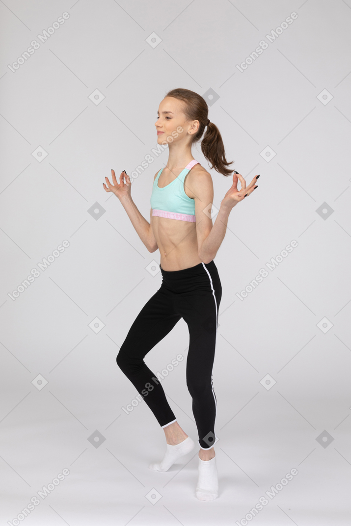 Vista de três quartos de uma adolescente em roupas esportivas separando as pernas