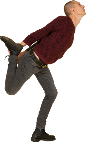 Вид сбоку на молодого человека в красном пуловере, растягивающего ногу