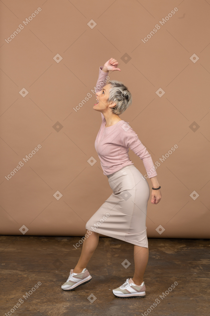 Vista lateral de una mujer emocional en ropa casual posando con el brazo levantado