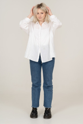 Front view of a blonde female raising hands and touching hair while looking down