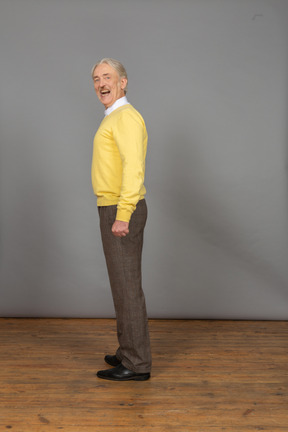 Seitenansicht eines lächelnden mannes in einem gelben pullover mit offenem mund, der kamera betrachtet