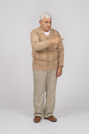 Front view of an old man in casual clothes poinitng with finger