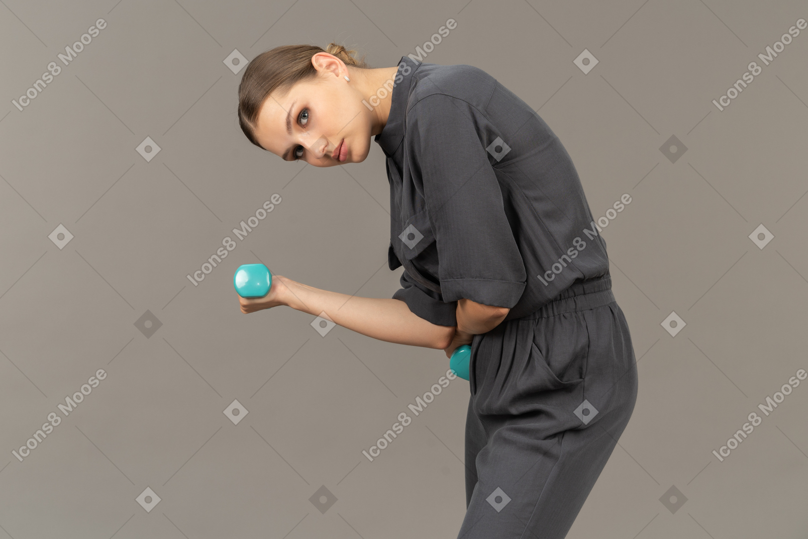 Side view of young woman in a jumpsuit doing exercises with dumbbells