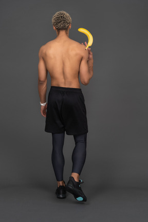 Vista posterior de un joven afro sosteniendo el plátano