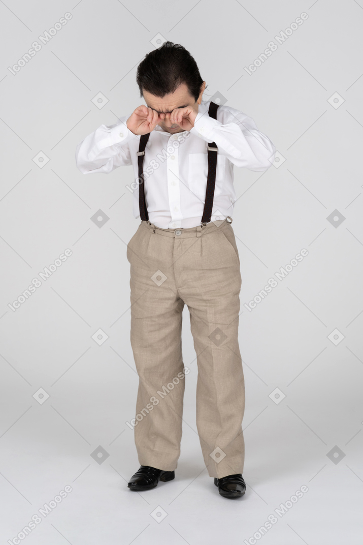 Man in suspenders rubbing eyes