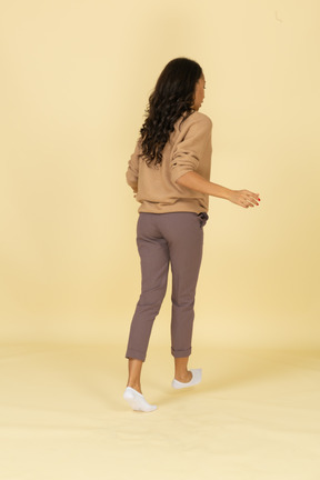 Vista posterior de tres cuartos de una mujer joven caminando de piel oscura