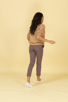 Three-quarter back view of a dark-skinned walking young female