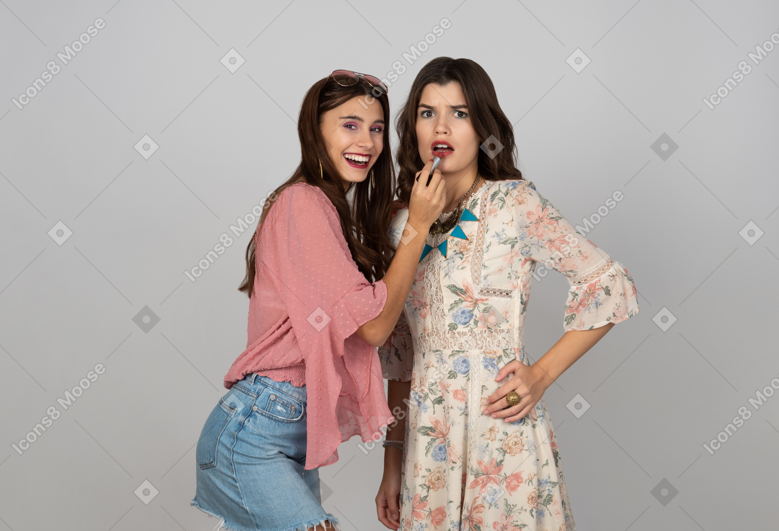 Cheerful young girl putting on lipstick on her friend's lips